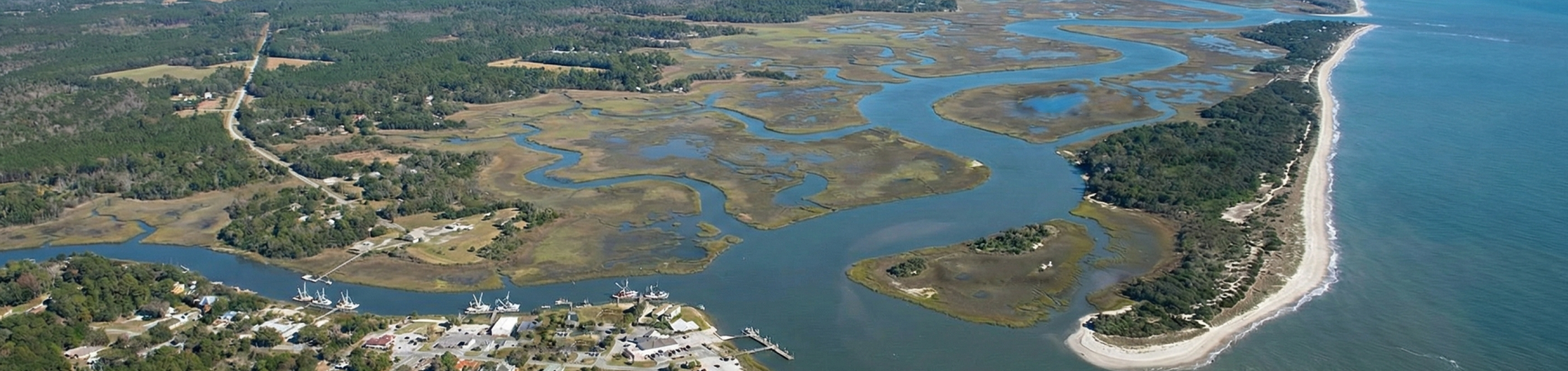 Aerial view of winding river meeting ocean along a grassy coastline.